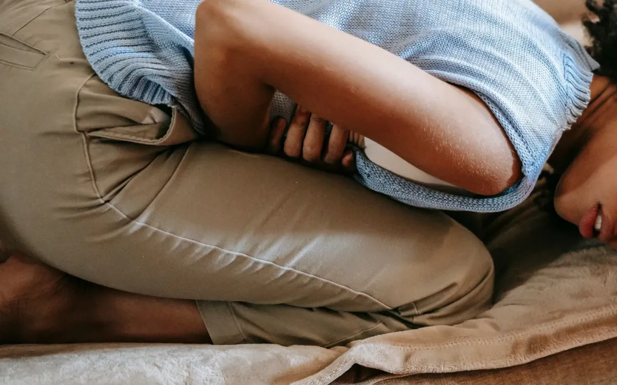 Femme recroquevillée sur un canapé, les bras autour du ventre