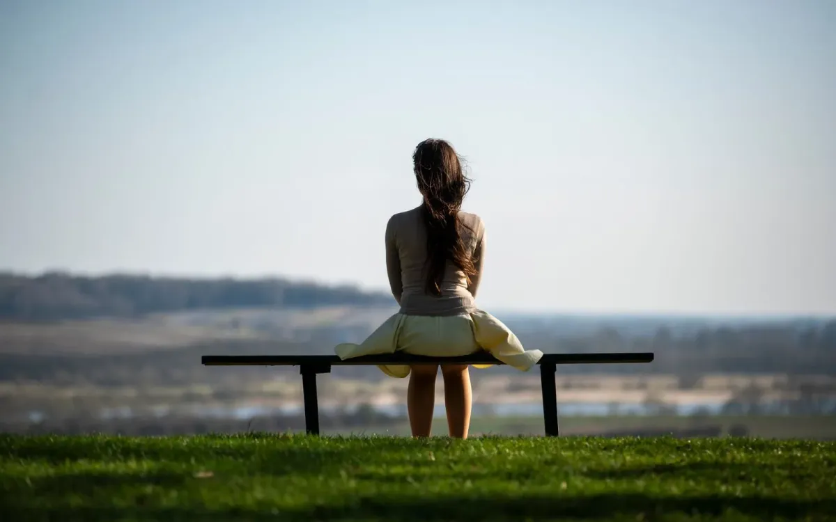 Femme assise seule sur un banc, face à l'horizon