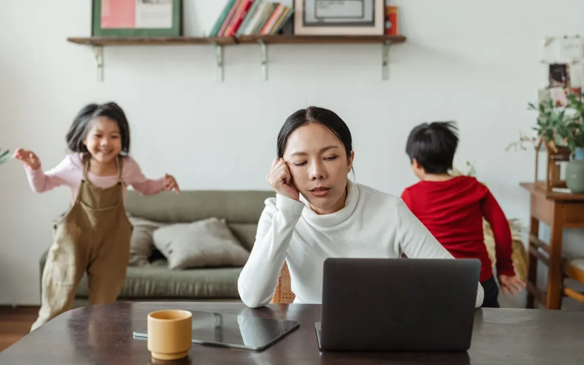 Mère débordée devant son ordinateur pendant que ses enfants jouent
