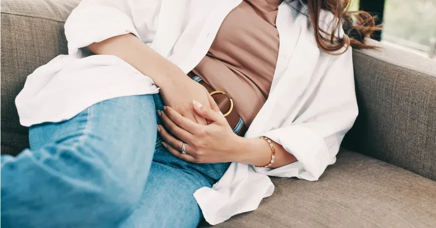 Femme assise sur un canapé, les mains posées sur un ventre tendu