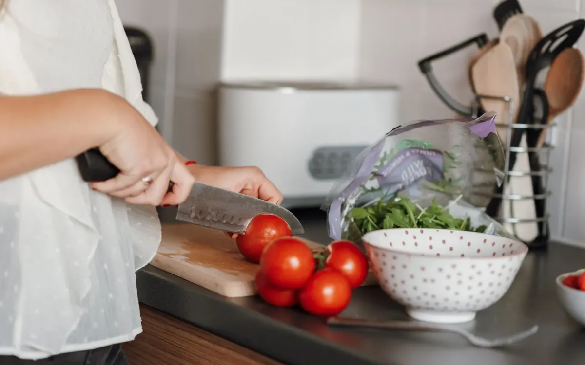 Une femme tranche des tomates dans sa cuisine, salade et légumes frais à côté