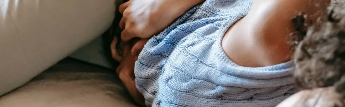 Femme allongée sur un canapé, les mains serrées sur le bas du ventre pendant des règles douloureuses