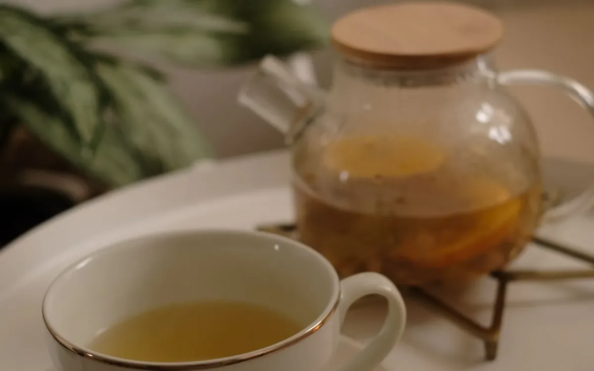 Théière en verre et tasse de tisane posées sur un plateau clair