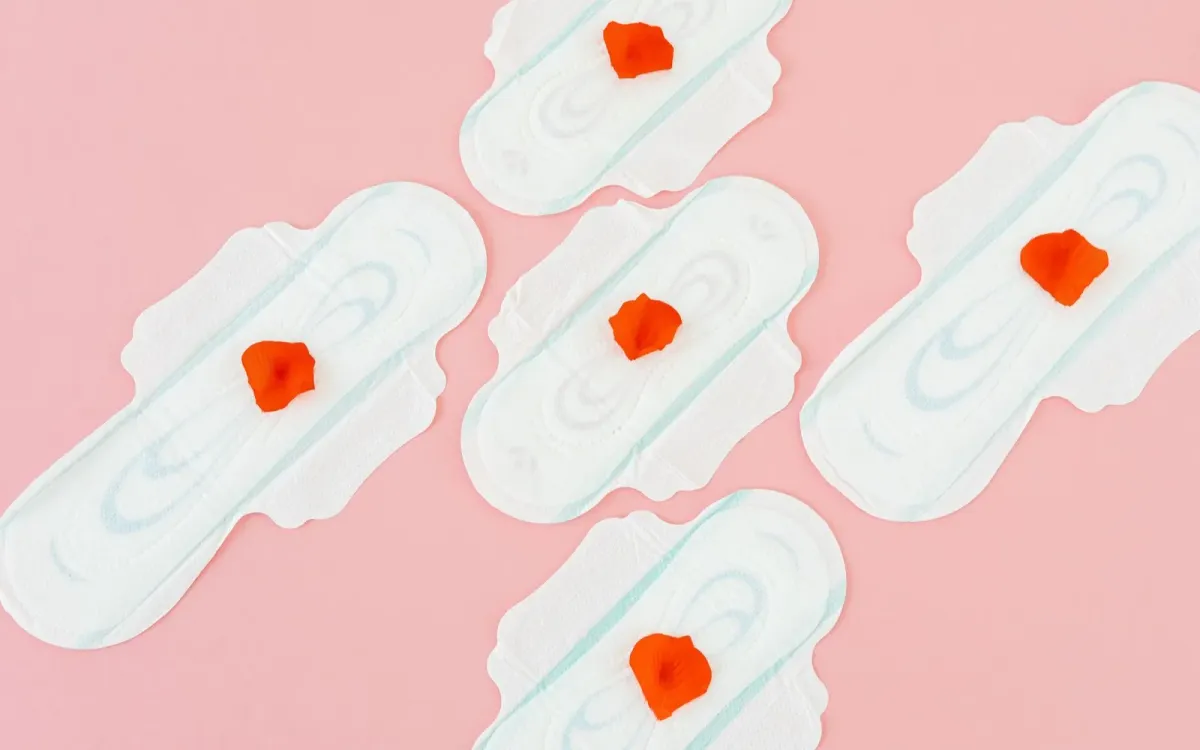 Des serviettes hygiéniques et des pétales rouges sur fond rose