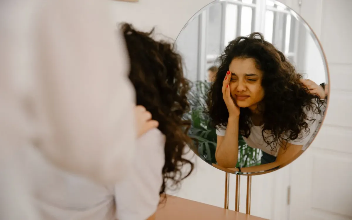 Une jeune femme se regarde dans un miroir, entre doute et questionnement
