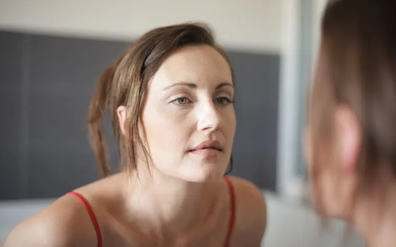 Femme qui observe son reflet dans le miroir de la salle de bain, l'air pensif