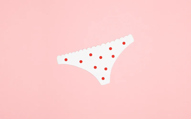 Culotte découpée dans du papier blanc, semée de pois rouges, posée sur un fond rose pâle