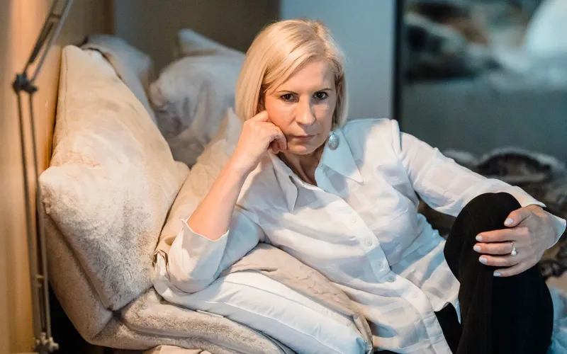 Femme d'une cinquantaine d'années, pensive, adossée aux coussins de son lit