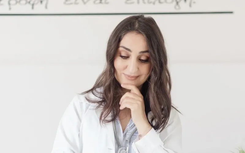 Femme en blouse blanche qui réfléchit, la main sous le menton, le regard baissé vers ses notes